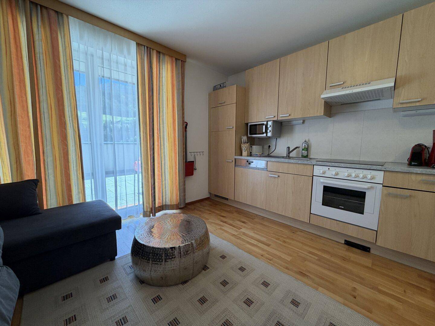 Offener Wohnbereich mit Küchenzeile, Sofa und Zugang zur Terrasse, hell und funktional.