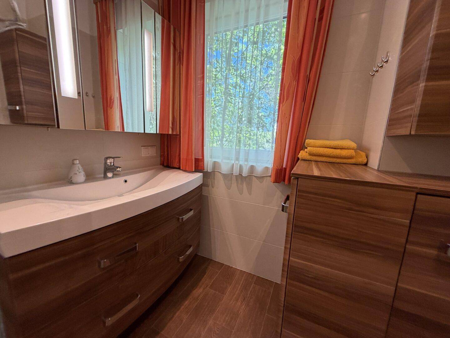 Modernes Badezimmer mit Holzwaschtisch, Spiegelschrank und Fenster mit Blick ins Grüne.