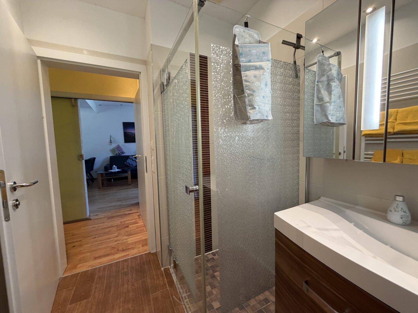 Badezimmer mit moderner Glasdusche, Holzwaschtisch und Zugang zum Wohnbereich.