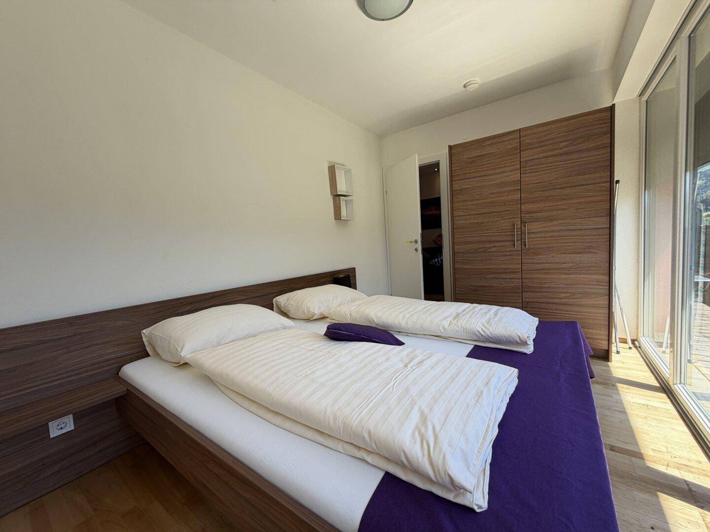 Geräumiges Schlafzimmer mit Doppelbett, Holzboden und großen Fenstern für viel Tageslicht.