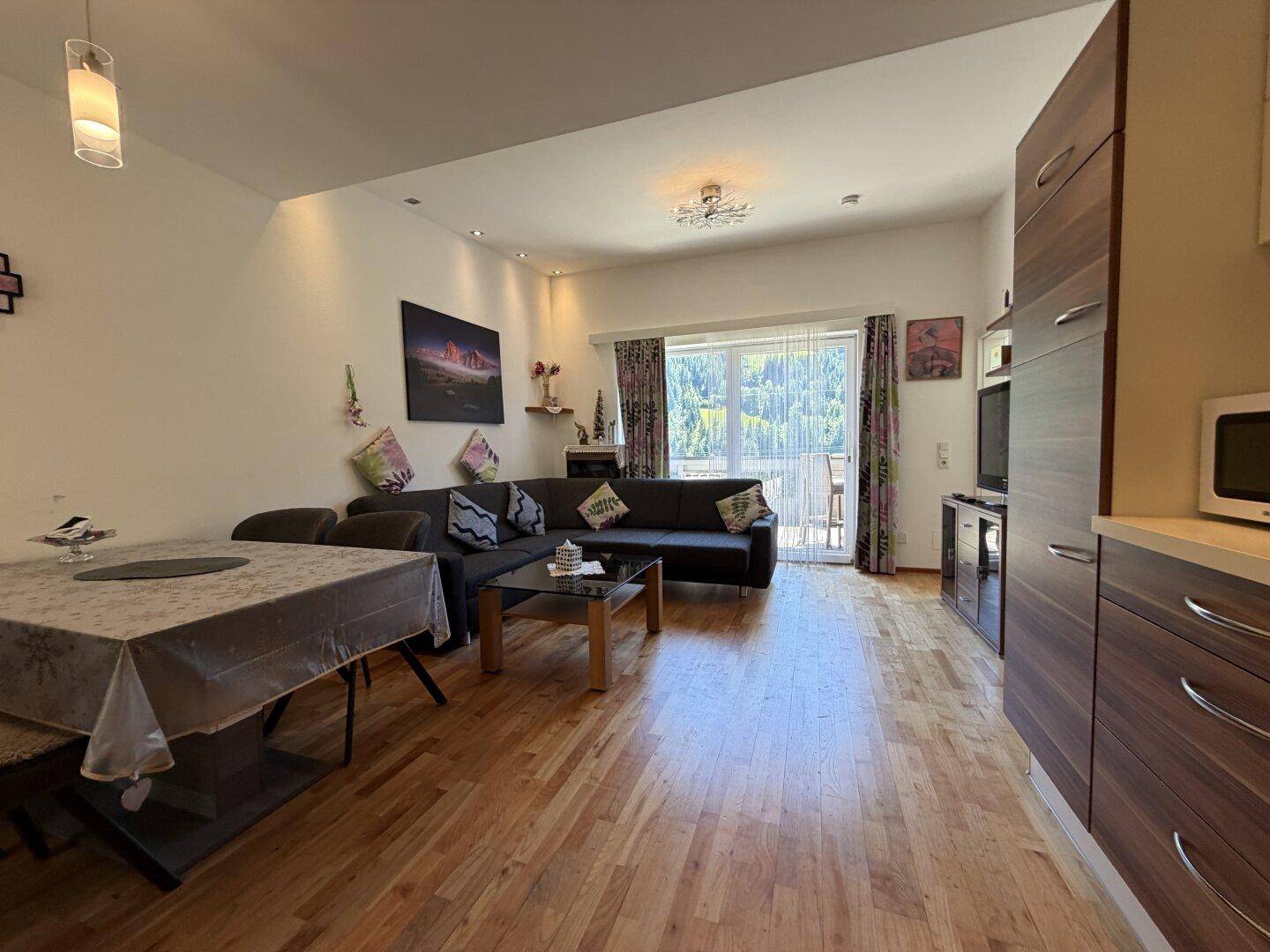Heller Wohn-Essbereich mit Holzboden, großem Sofa und Zugang zum Balkon, modern eingerichtet.