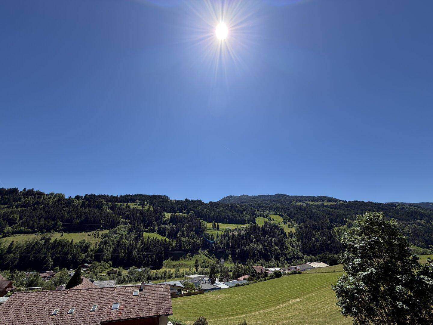 Panoramablick über die grüne Landschaft und bewaldete Berge unter strahlendem Sonnenschein.