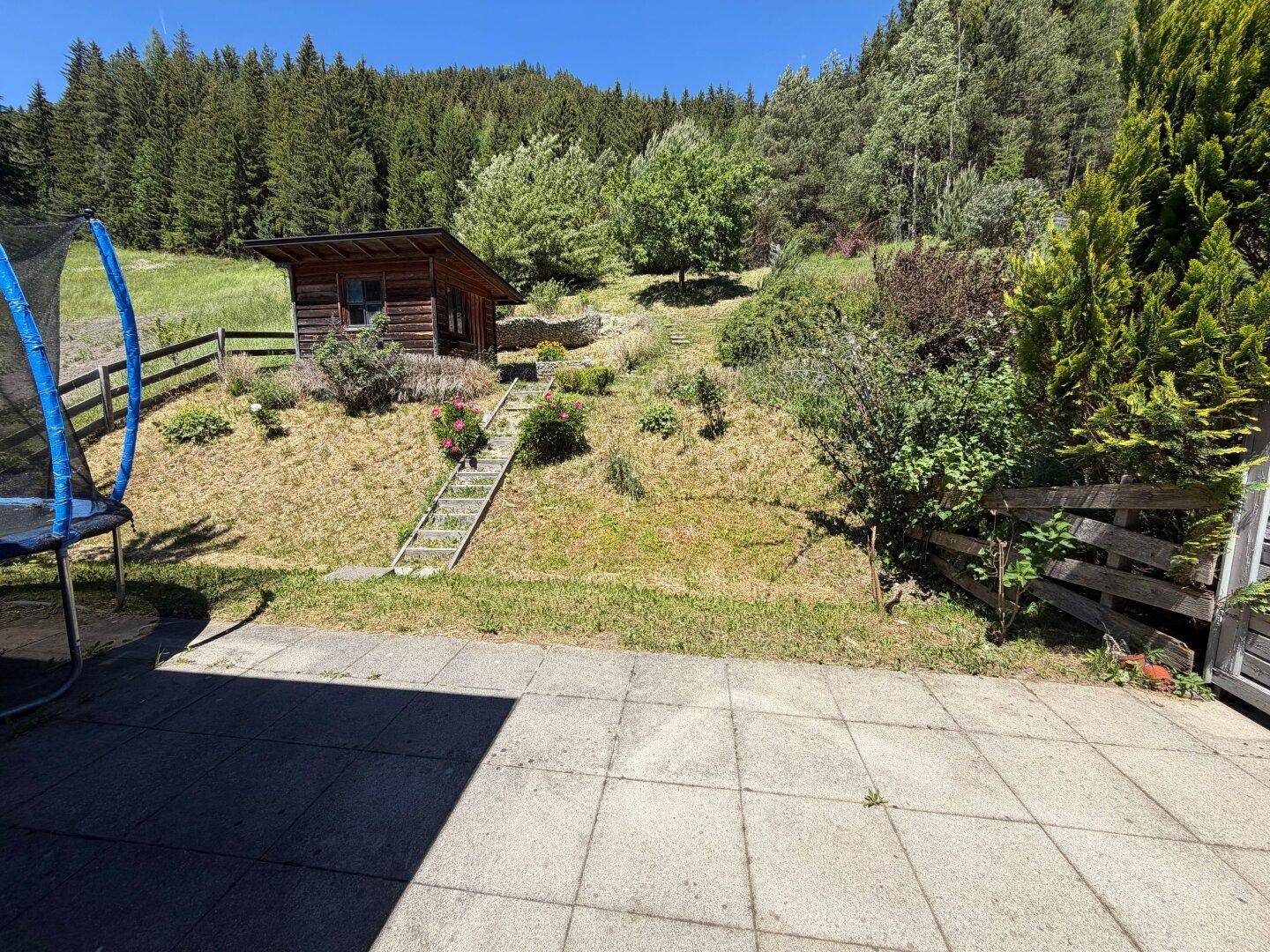 Naturbelassener Gartenbereich mit Holzschuppen und Treppe zum Hang, umgeben von Wald.