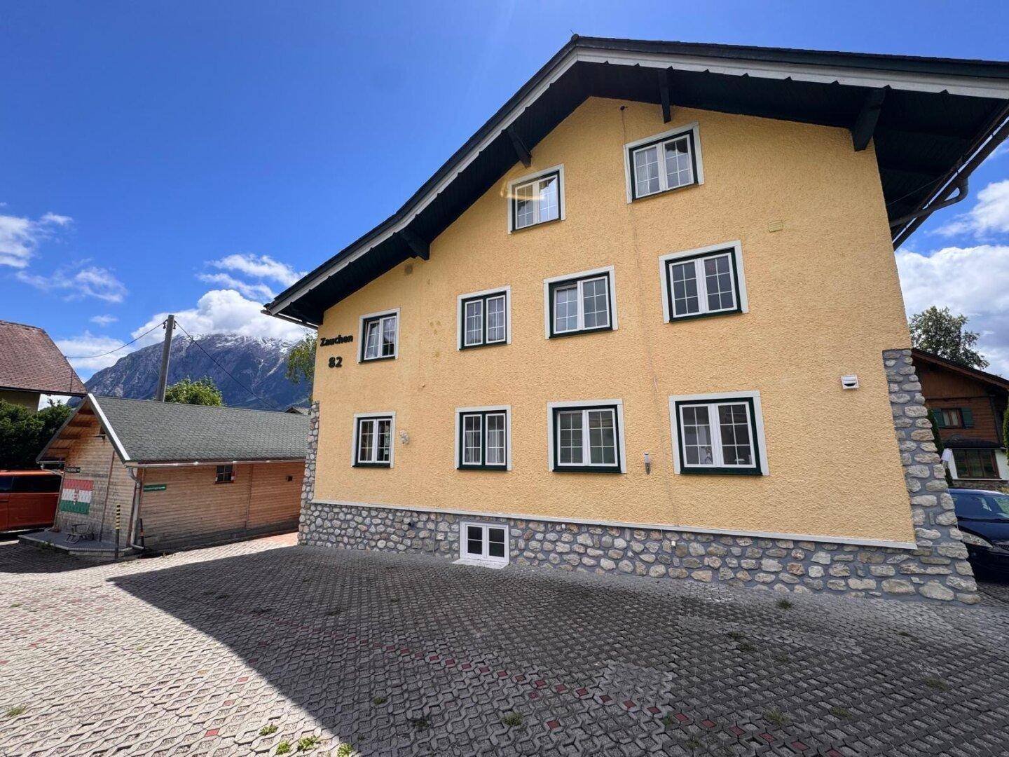 Seitenansicht des Hauses mit gepflastertem Parkplatz und Blick auf die umliegende Berglandschaft.