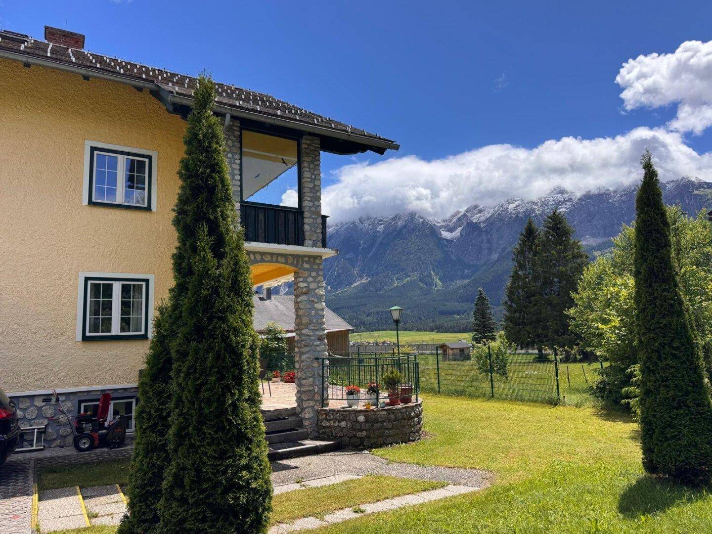 Seitenansicht des Hauses mit gepflegtem Garten und beeindruckendem Panoramablick auf die Berge.