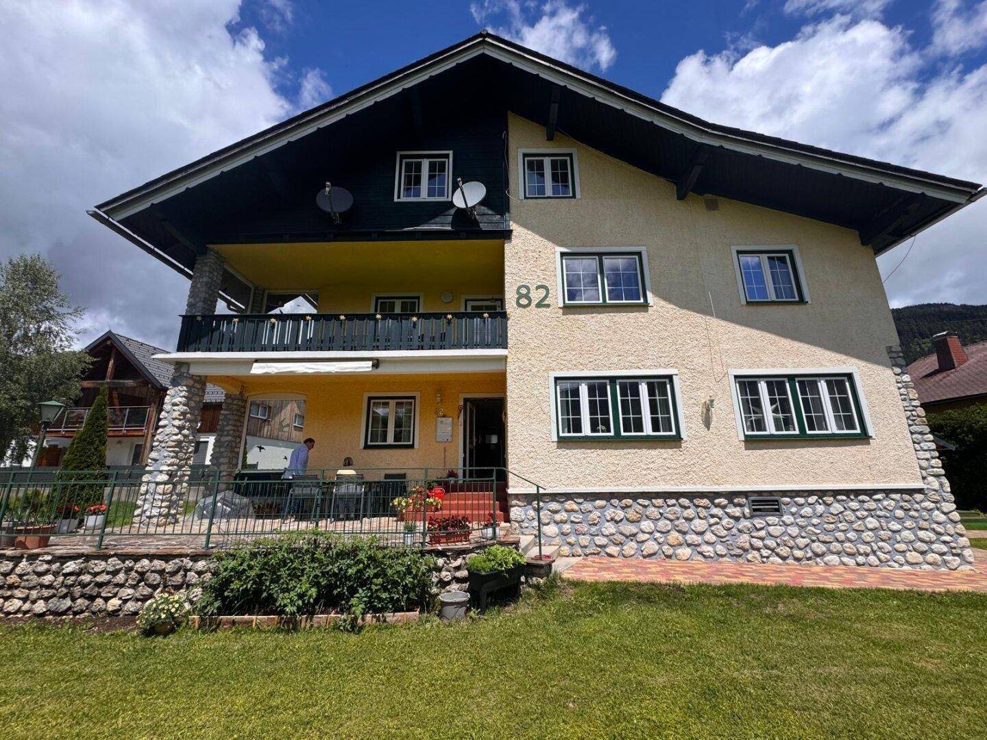 Vorderansicht eines traditionellen Hauses mit Balkon und Steinsockel in sonniger Lage.