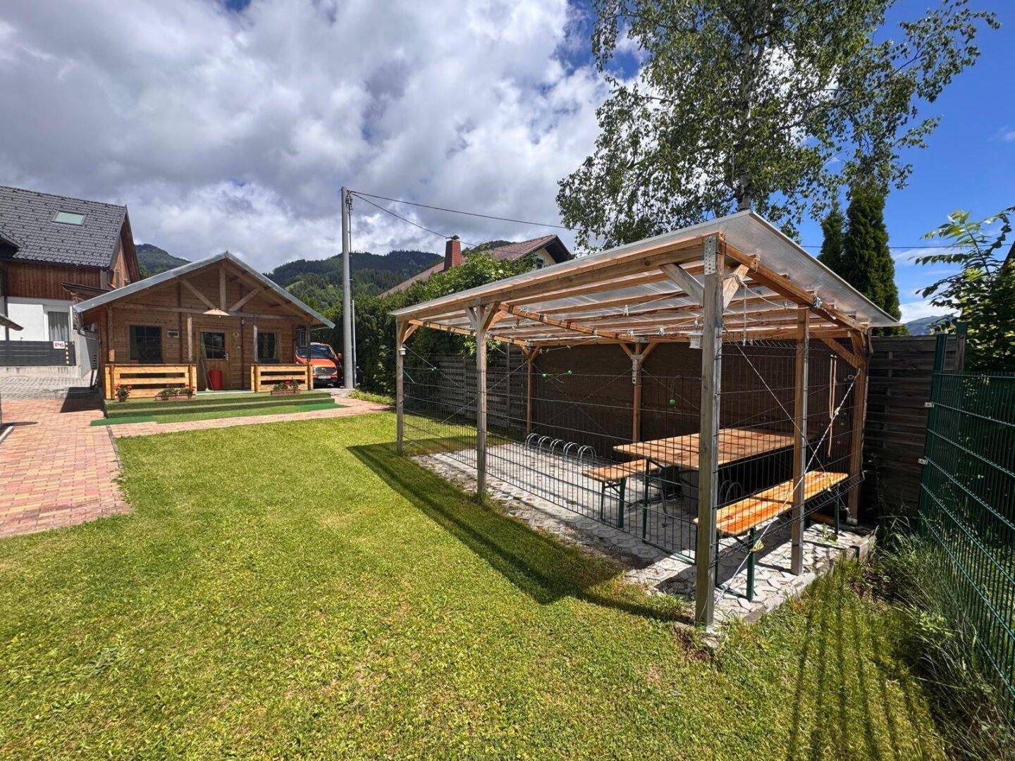 Überdachter Sitzbereich im Garten mit Holztischen und Bänken, ideal für gesellige Stunden.