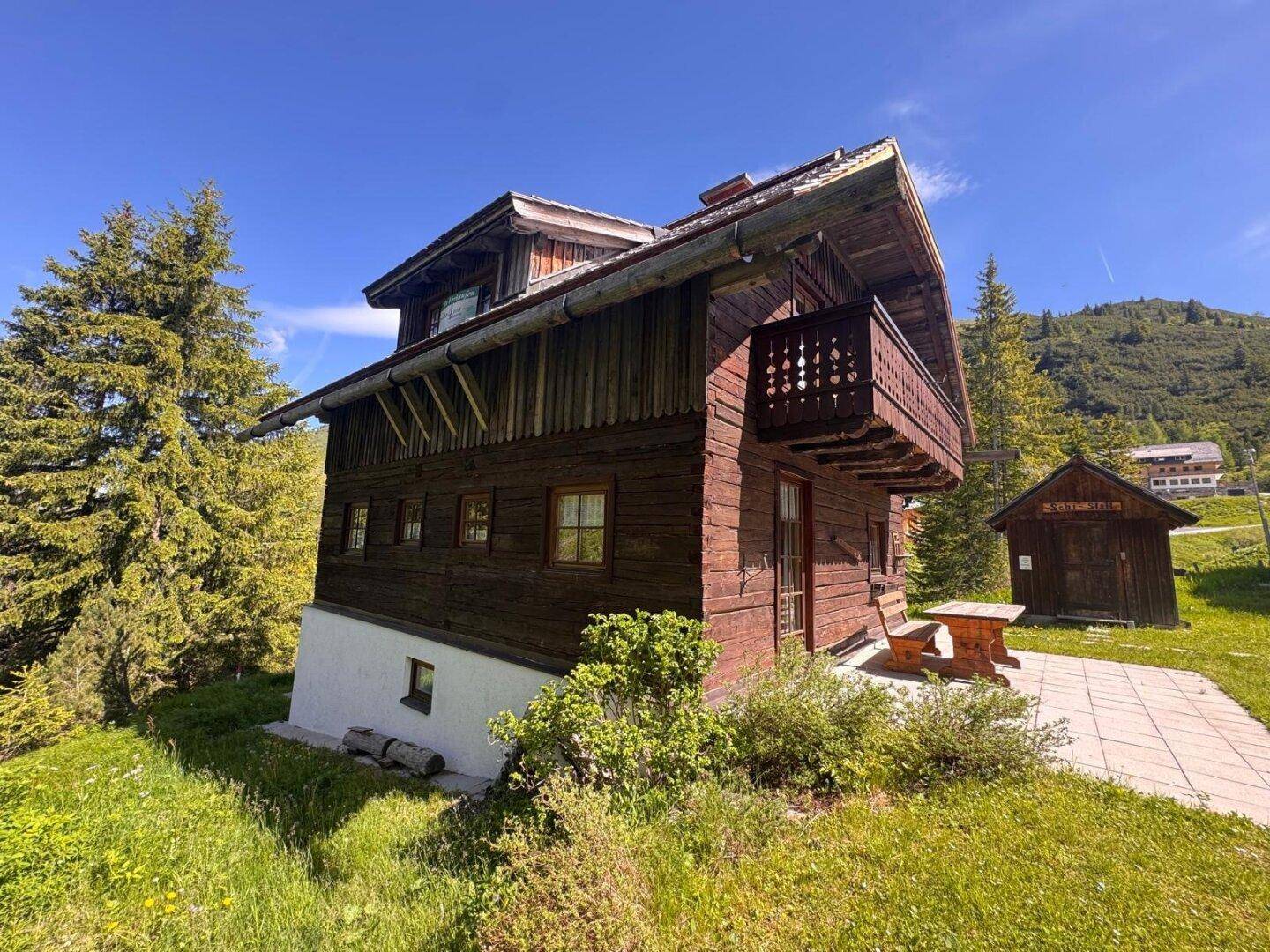 Ansicht des traditionellen Holzchalets mit Holzbalkon und gepflegter Grünfläche in sonniger Berglage.
