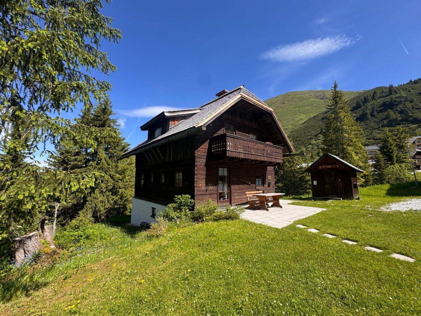 Seitenansicht des Holzchalets mit Balkon, gepflasterter Terrasse und Picknicktisch in Hanglage.