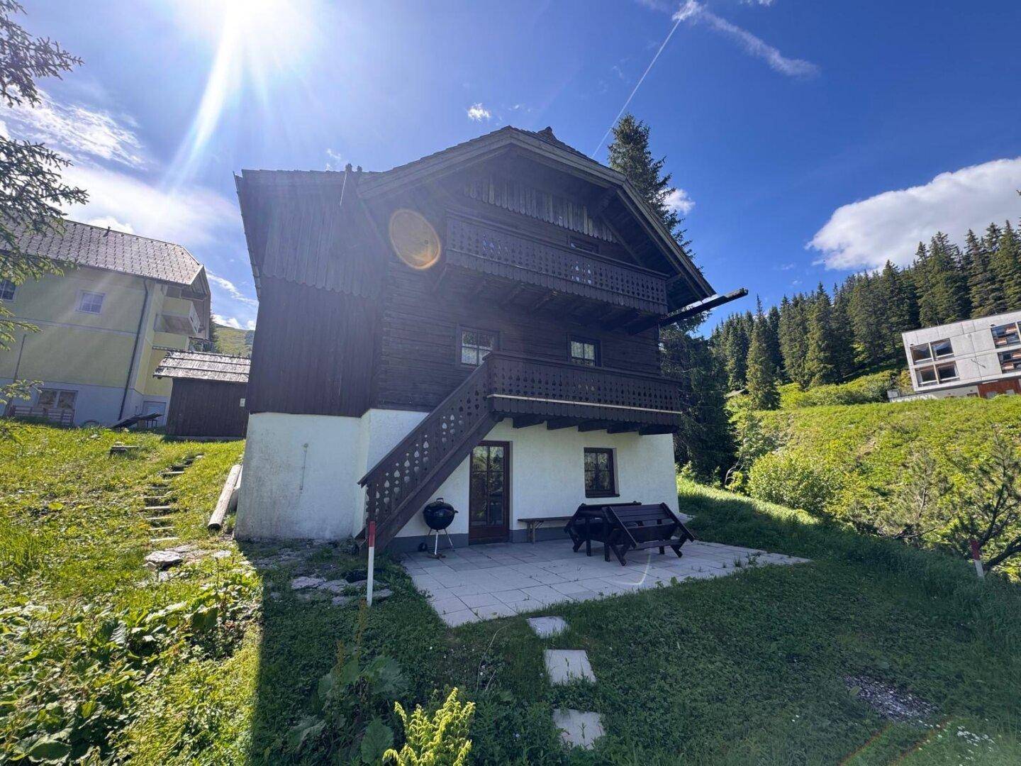 Rückseite des Holzchalets mit Außentreppe, Balkon und Terrasse mit Grillbereich und Sitzgelegenheiten.