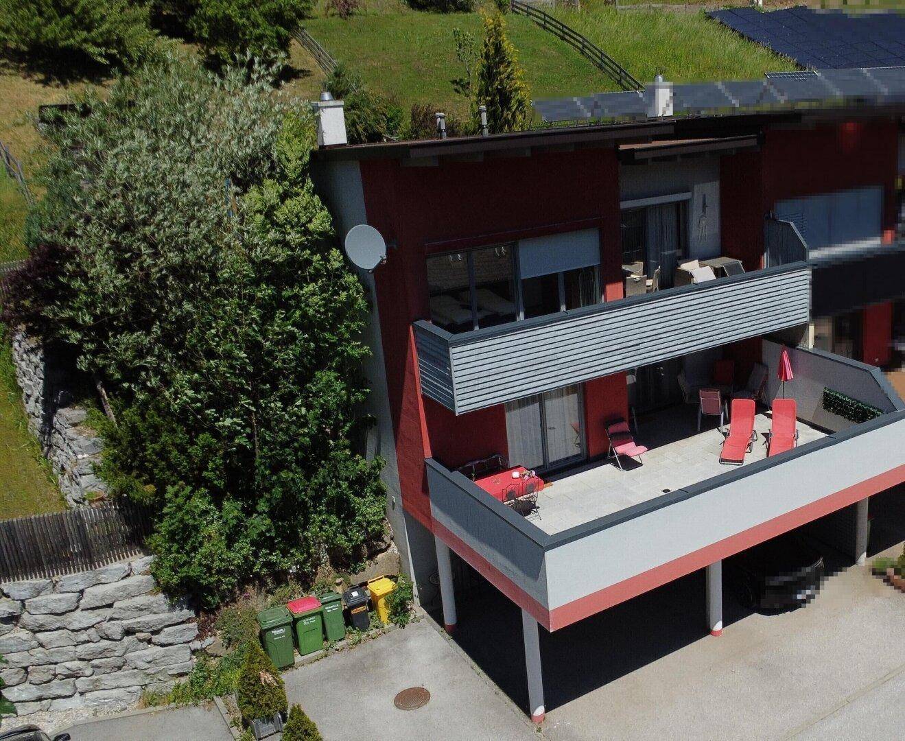 Ansicht einer modernen Wohnanlage mit Balkonen, einer möblierten Terrasse und angrenzendem Grünbereich.
