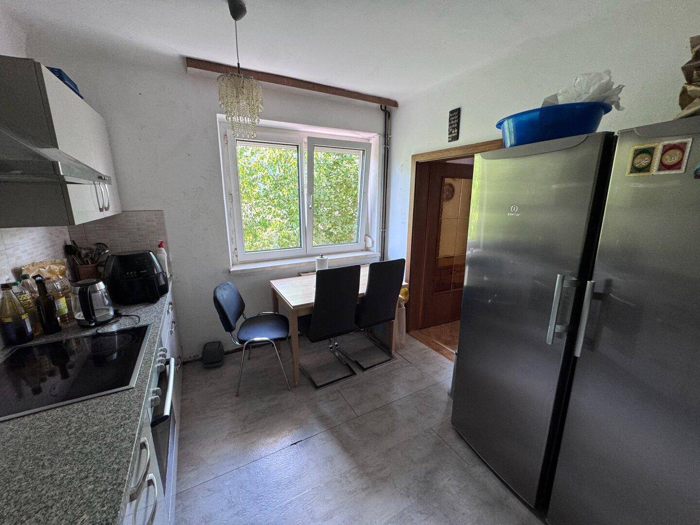 Geräumige Wohnküche mit Esstisch am Fenster, modernen Geräten und Fliesenboden.