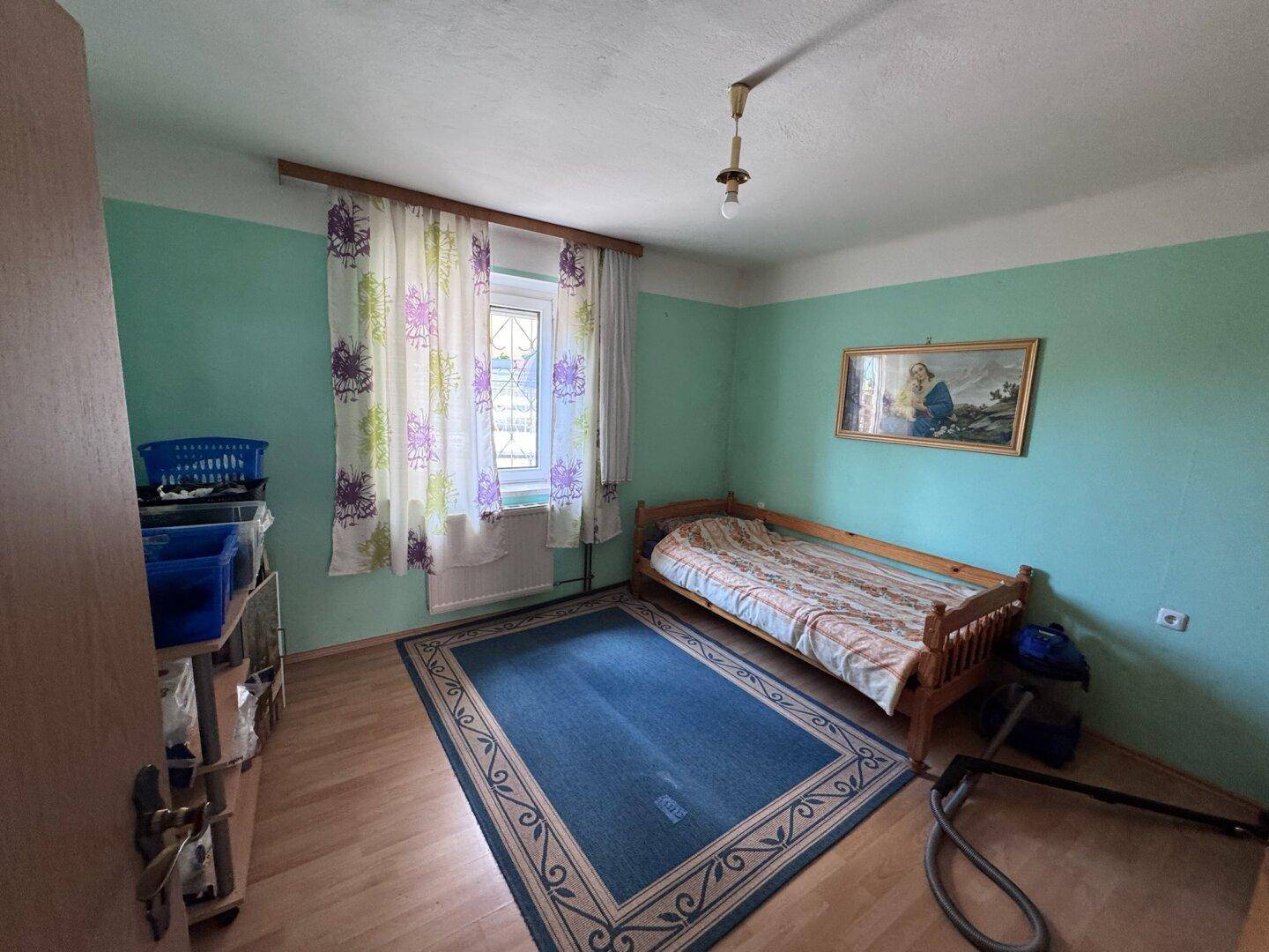 Schlafzimmer mit grün gestrichenen Wänden, Holzbett und Teppichboden.