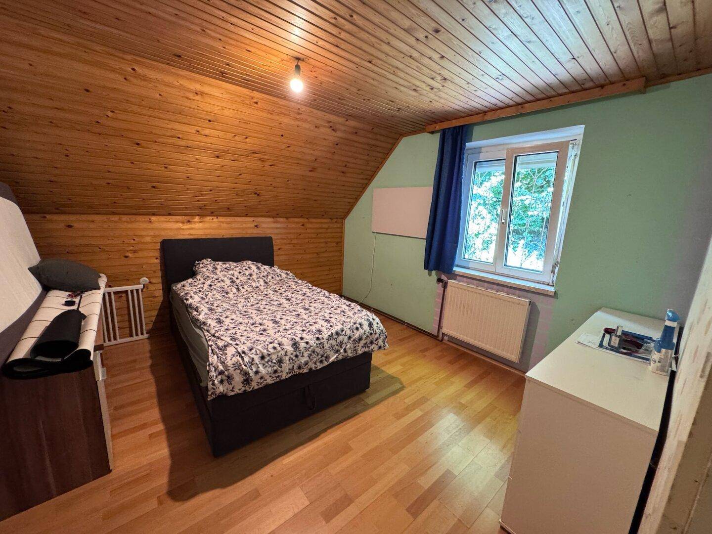 Dachschlafzimmer mit Holzverkleidung an der Decke, Holzboden und schrägen Wänden.