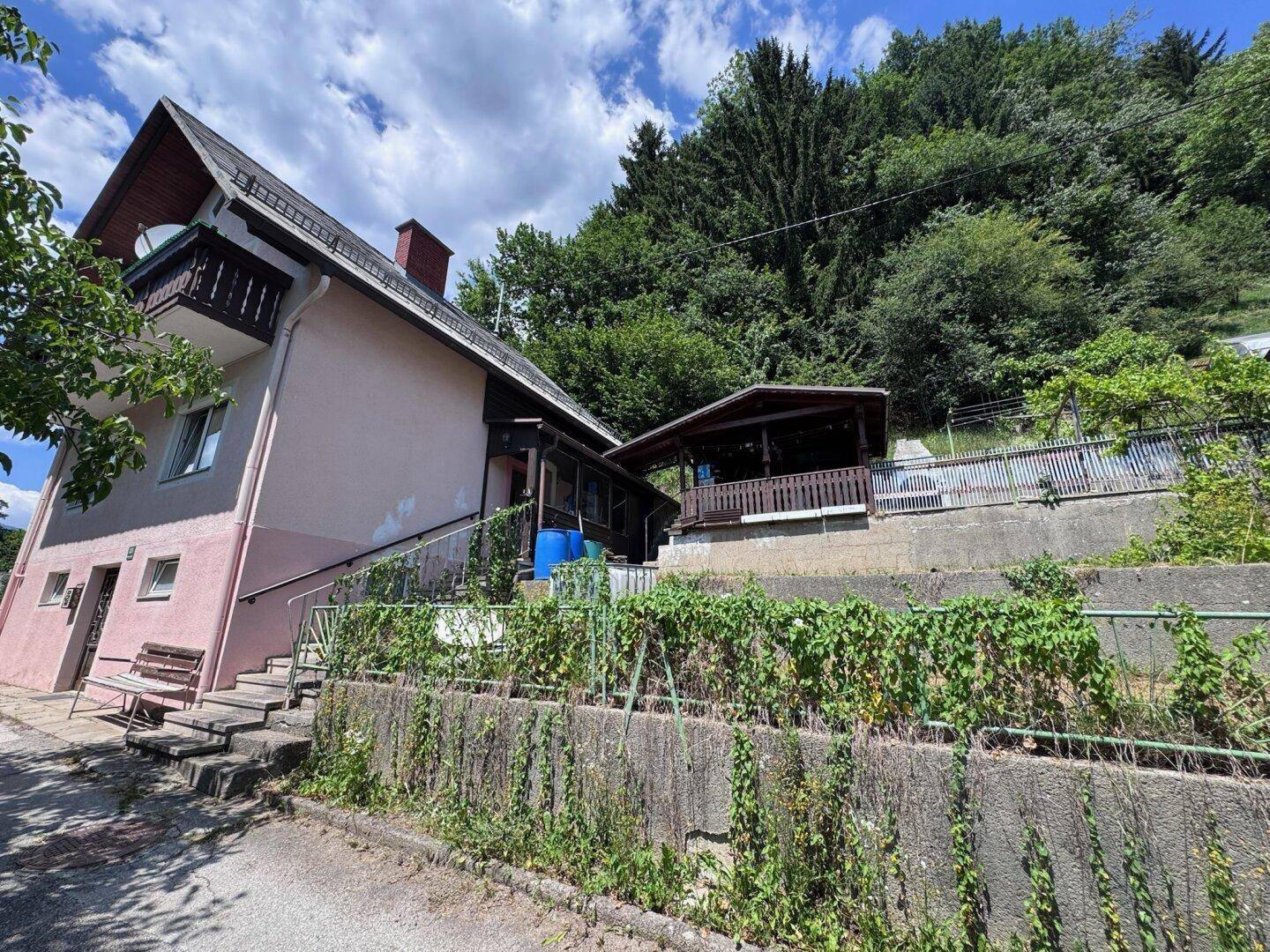 Hausansicht von der Seite mit Außentreppe, Gartenbereich und einem kleinen Holzhaus im Hintergrund.