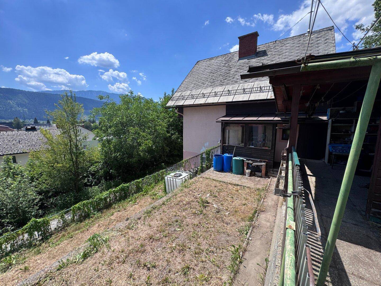 Seitliche Ansicht des Hauses mit einem terrassierten Gartenbereich und Blick auf die Berge.