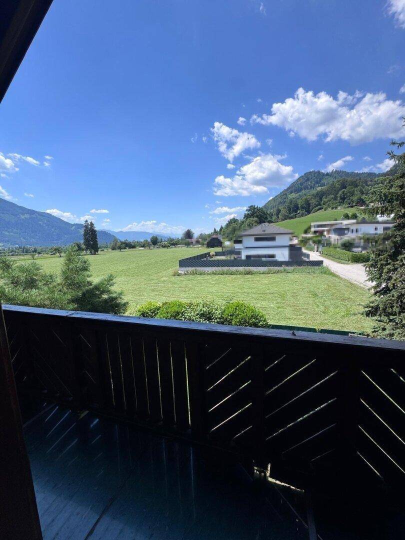Balkon mit Holzbalken und weitem Blick über grüne Felder und die umliegende Berglandschaft.