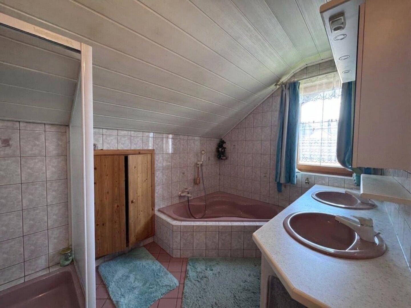 Badezimmer mit rosa Fliesen, Eckbadewanne, Doppelwaschbecken und Dachschräge.