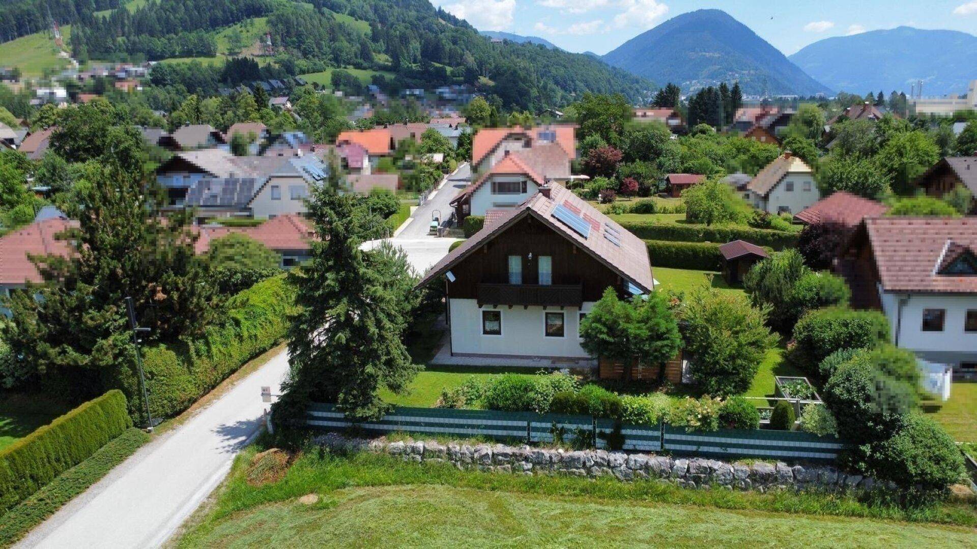 Ländliche Umgebung mit Einfamilienhaus, umgeben von viel Grün und Bergen im Hintergrund.