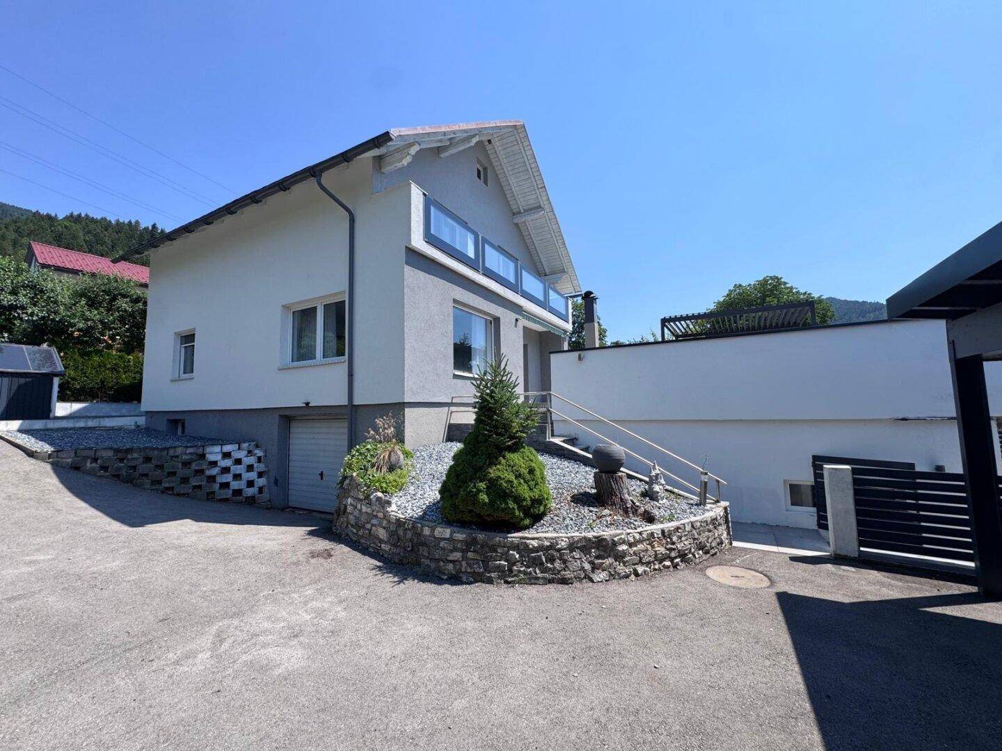 Einfamilienhaus mit moderner Architektur, Balkon und gepflasterter Zufahrt an einem sonnigen Tag.