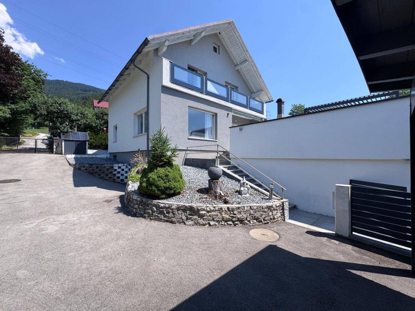 Modernes Einfamilienhaus mit heller Fassade, Balkon und gepflegter Außenanlage unter blauem Himmel.