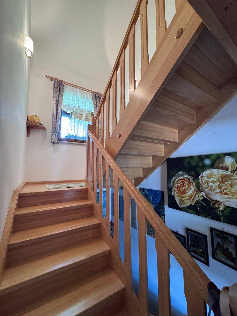 Massive Holztreppe mit Geländer und Fenster, die die Stockwerke verbindet.