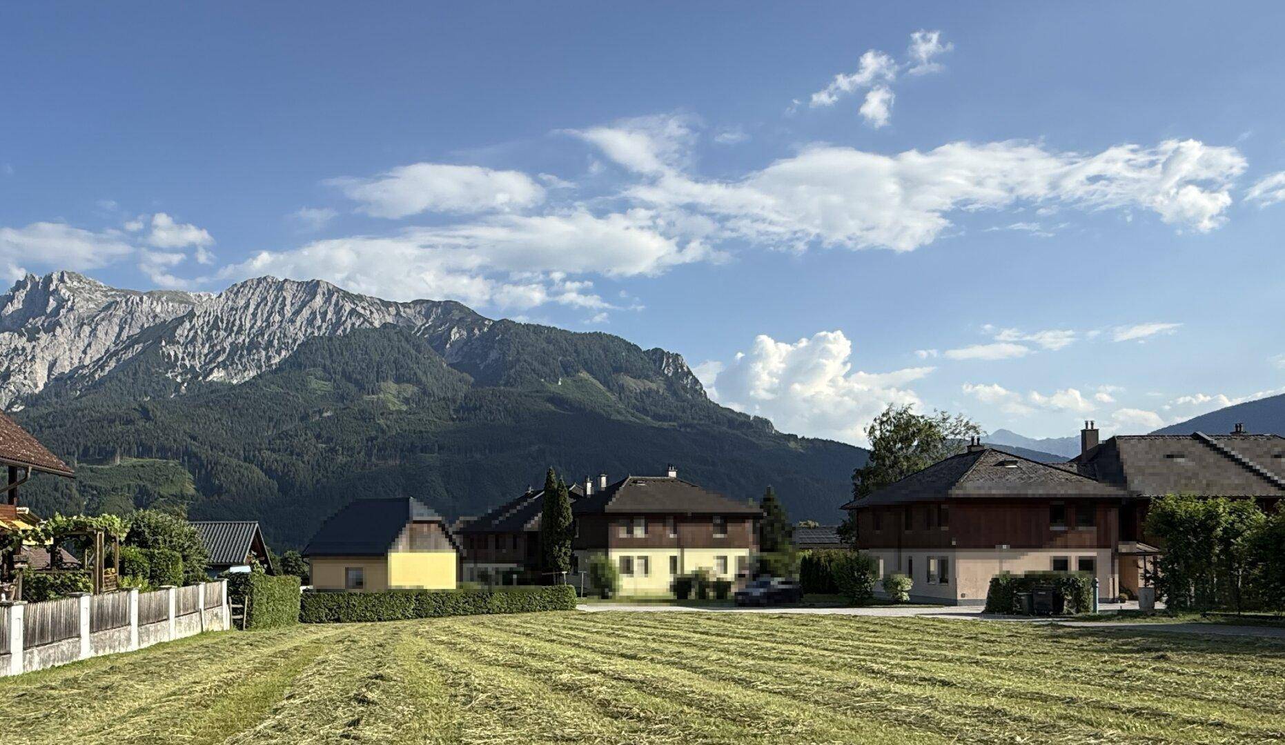 Ländliche Szenerie mit gemähten Wiesen, traditionellen Häusern und einer beeindruckenden Bergkulisse.