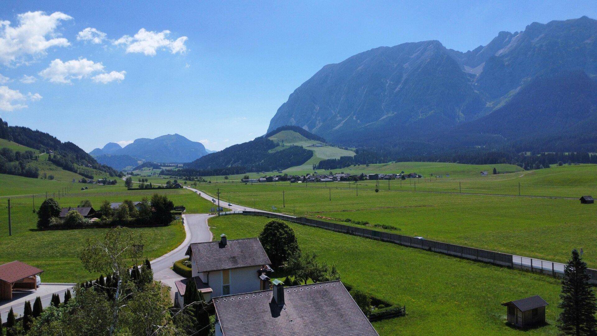 Weitläufige grüne Landschaft mit Bergen und einer Straße, die sich durch die Natur schlängelt.