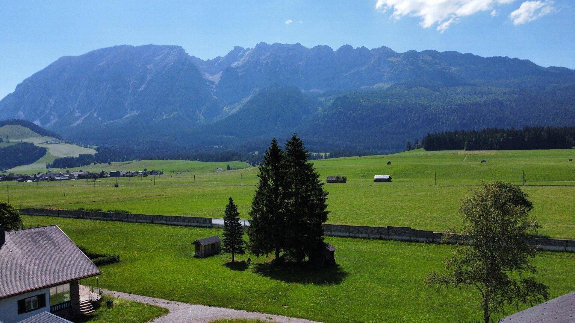 Atemberaubende Berglandschaft mit weiten grünen Feldern und vereinzelten Häusern unter blauem Himmel.