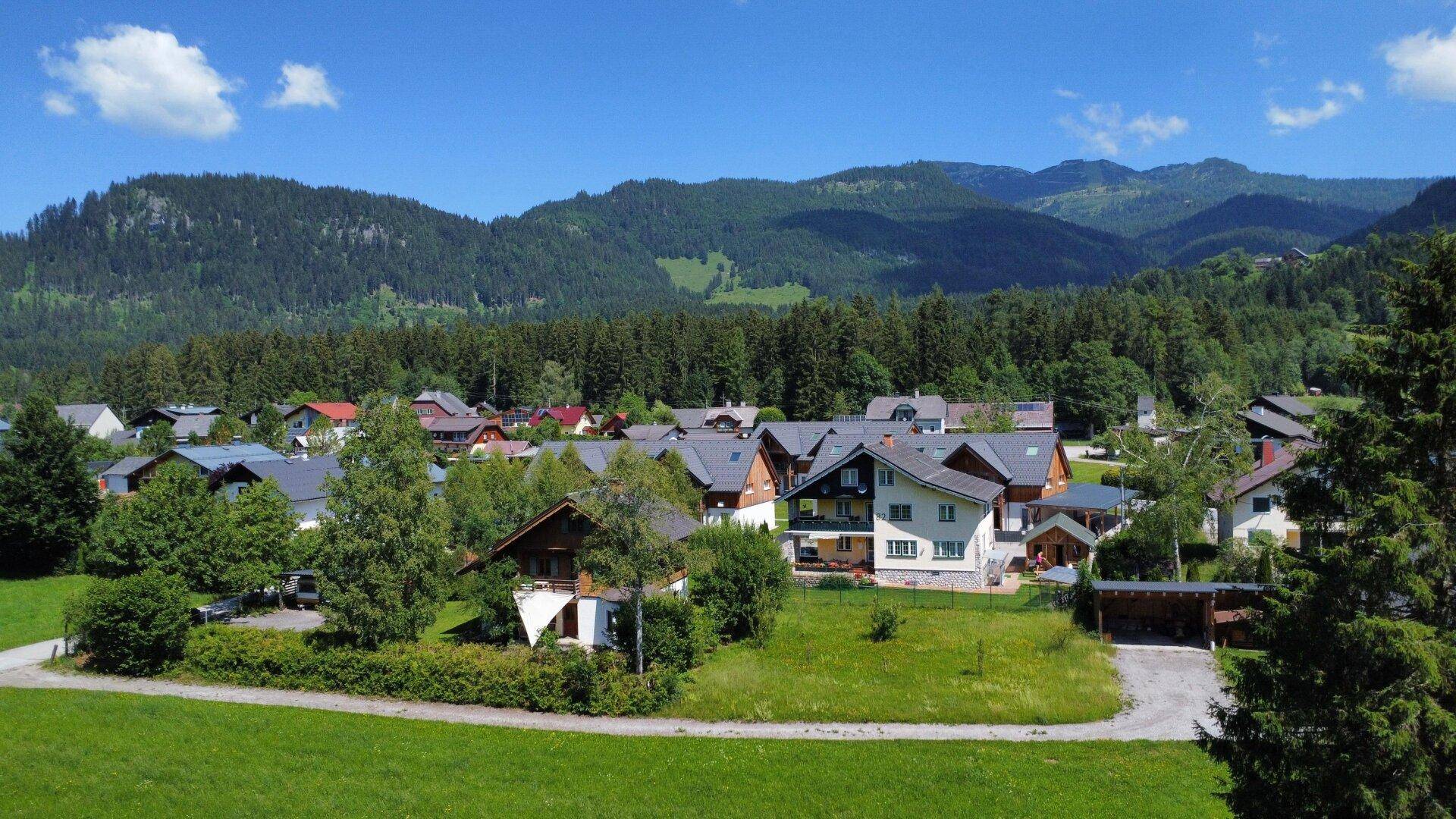 Malerisches Dorf in einem Tal, umgeben von grünen Hügeln und Wäldern unter blauem Himmel.