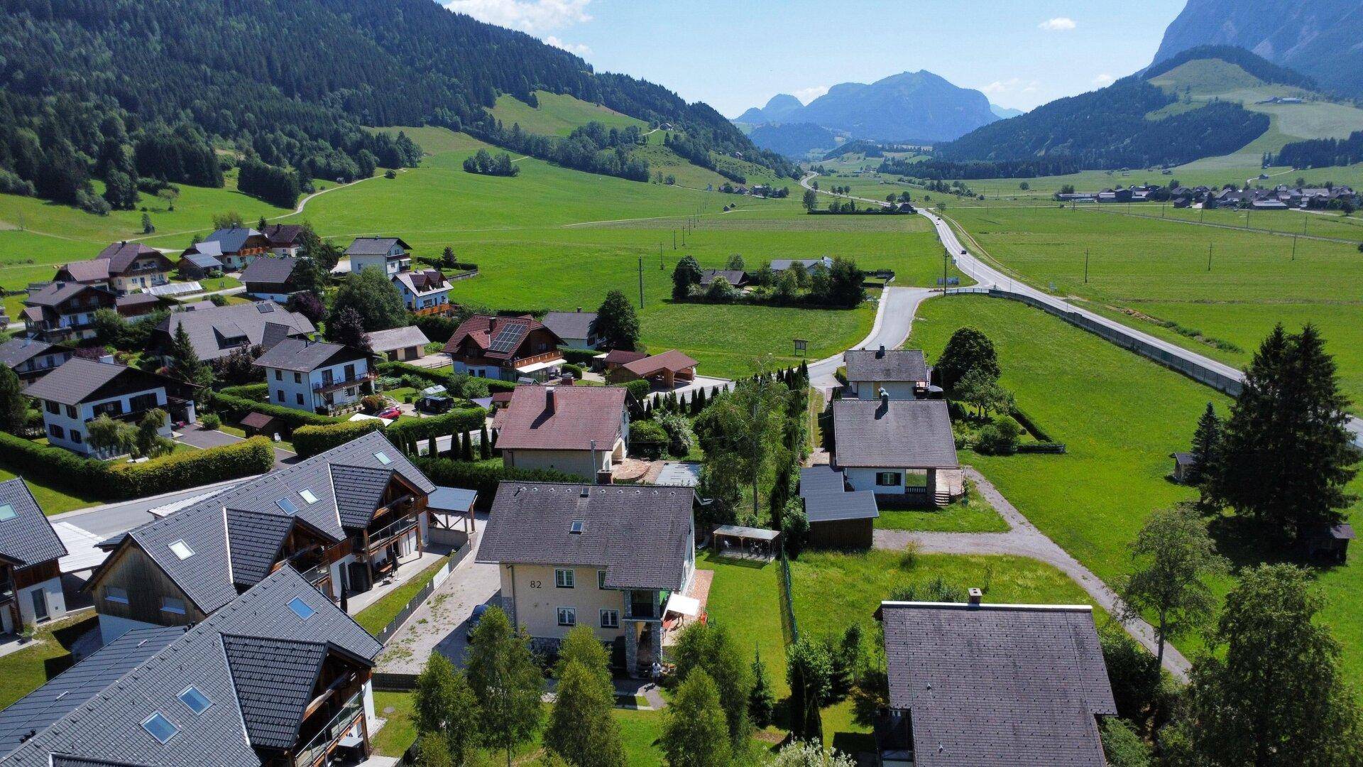 Luftaufnahme eines Wohngebiets in einem grünen Tal mit Häusern und Straßen.