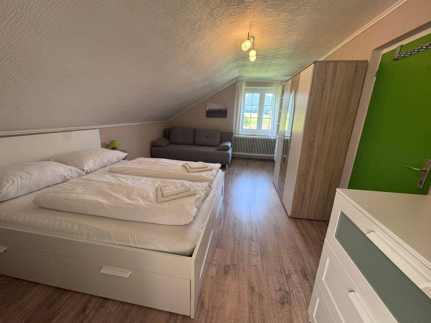 Gemütliches Schlafzimmer im Dachgeschoss mit Doppelbett, Sofa und Dachschräge.