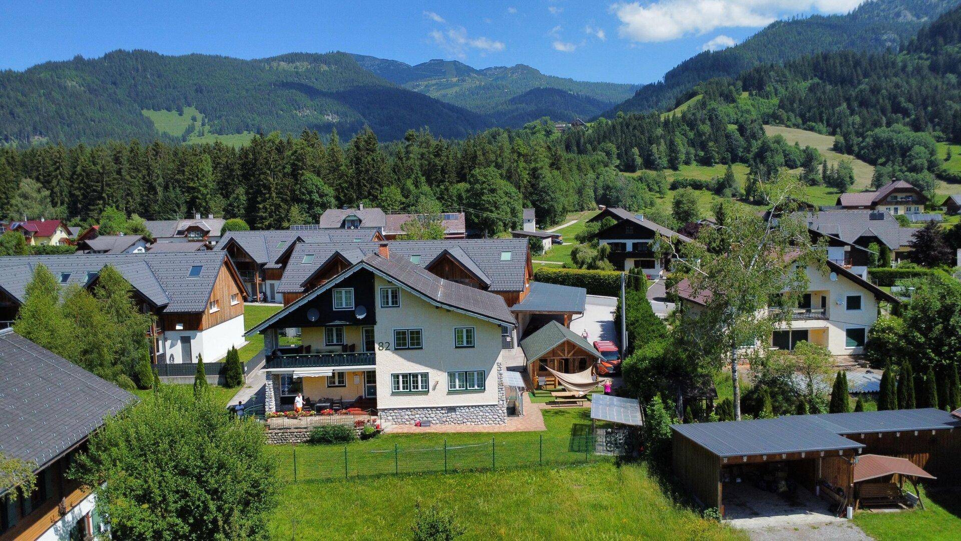 Malerische Wohnsiedlung in den Bergen mit grünen Wiesen und Wäldern unter blauem Himmel.