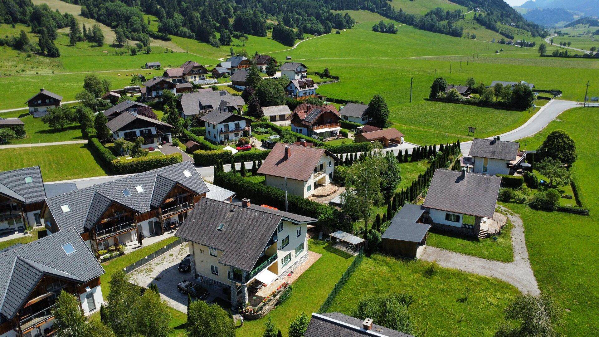 Weitläufige Wohnsiedlung eingebettet in grüne Hügel und Wälder mit beeindruckender Bergkulisse.