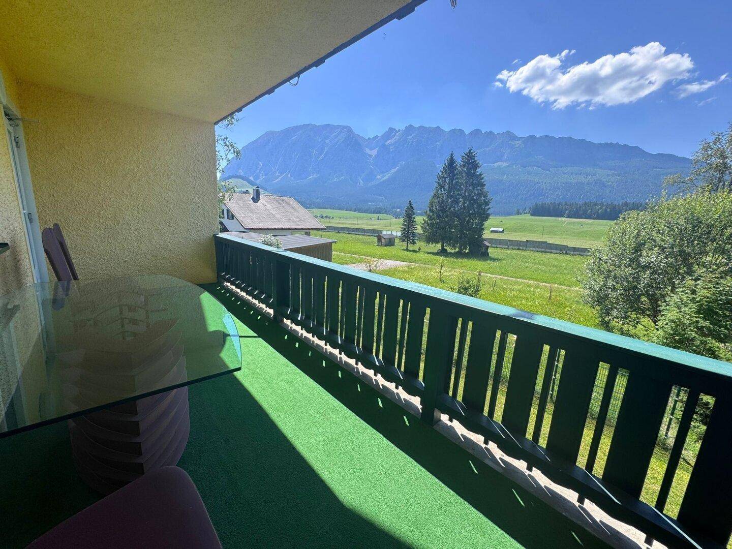 Balkon mit Kunstrasen, Esstisch und atemberaubendem Bergblick über grüne Felder.