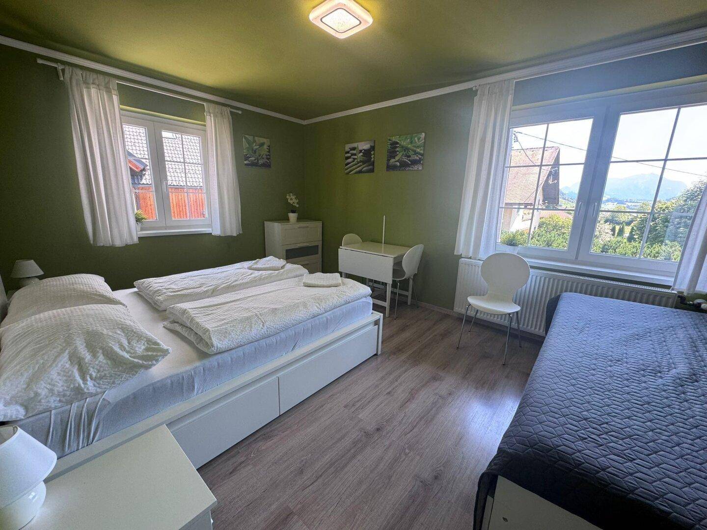 Helles Schlafzimmer mit zwei Einzelbetten, grünen Wänden und Blick auf die Landschaft.