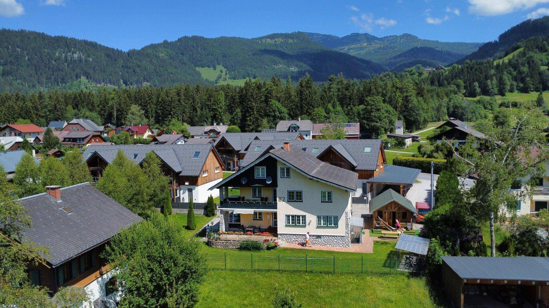 Idyllische Wohngegend mit Häusern, umgeben von üppiger Natur und einem weiten Bergpanorama.