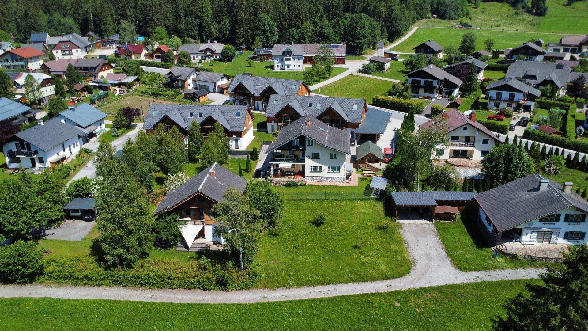 Weitläufige Ansicht einer Wohnsiedlung mit Häusern und Gärten in alpiner Landschaft.