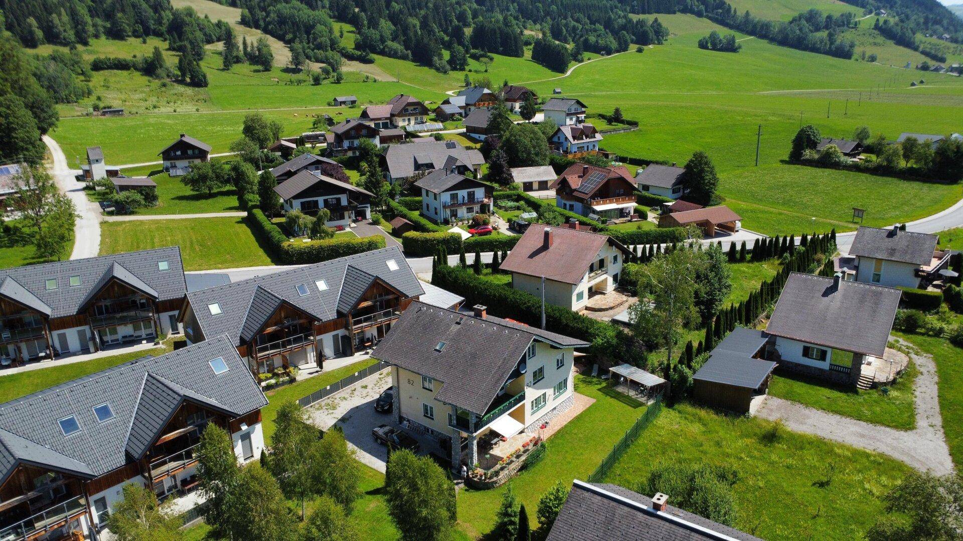 Luftaufnahme einer Wohnsiedlung mit Einfamilienhäusern und viel Grün in alpiner Landschaft.