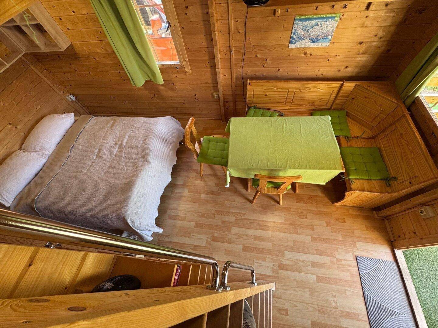 Gemütlicher Wohn- und Schlafbereich in einer Holzhütte mit Esstisch und Doppelbett.