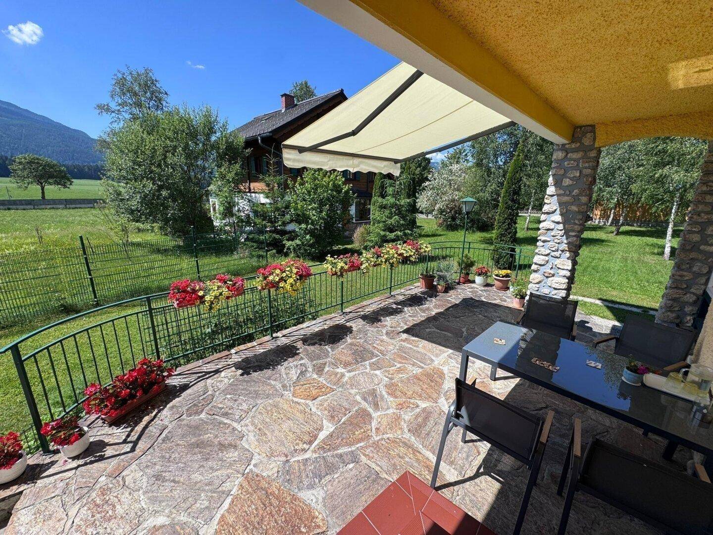 Sonnenterrasse mit Markise, Gartenmöbeln und weitem Blick auf die grüne Landschaft und Berge.