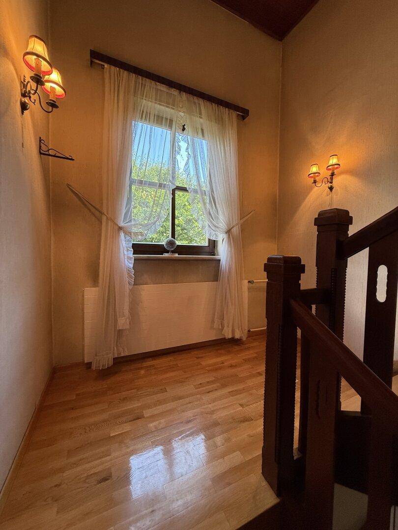 Heller Flur mit Holzboden, Fenster und einer eleganten Holztreppe, die in die oberen Stockwerke führt.