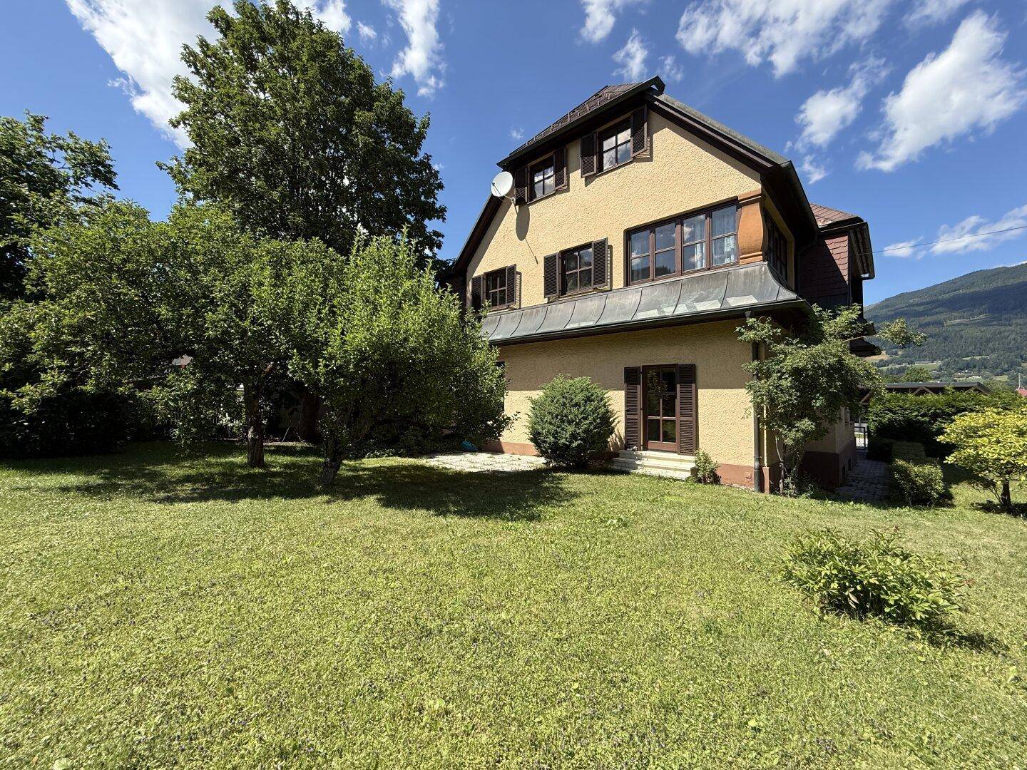 Rückansicht des Hauses mit großem Garten und malerischem Blick auf die umliegende Berglandschaft.