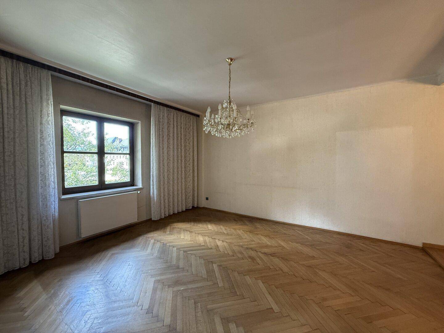 Großes, helles Zimmer mit Fischgrätparkett, einem großen Fenster und einem prächtigen Kristallleuchter.