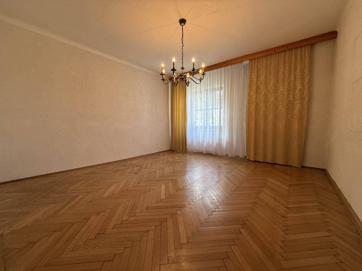 Elegantes Zimmer mit Fischgrätparkett, großen Fenstern und einem stilvollen Kronleuchter, bereit zur Gestaltung.