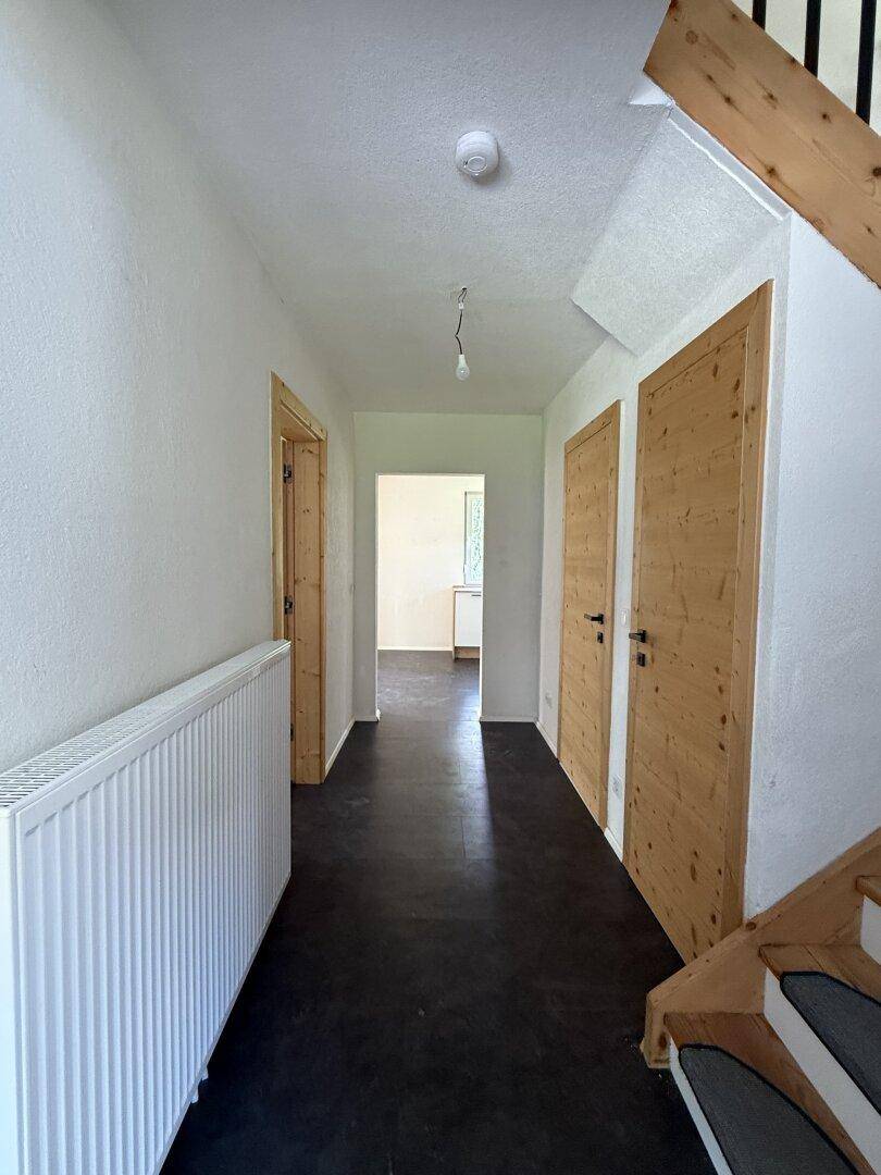Heller Flur mit dunklem Boden, Heizkörper und Holztüren, der zu den Zimmern führt.