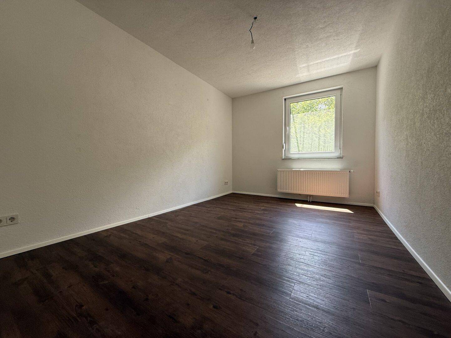 Geräumiges Schlafzimmer mit dunklem Laminatboden und Fenster, das viel Tageslicht hereinlässt.