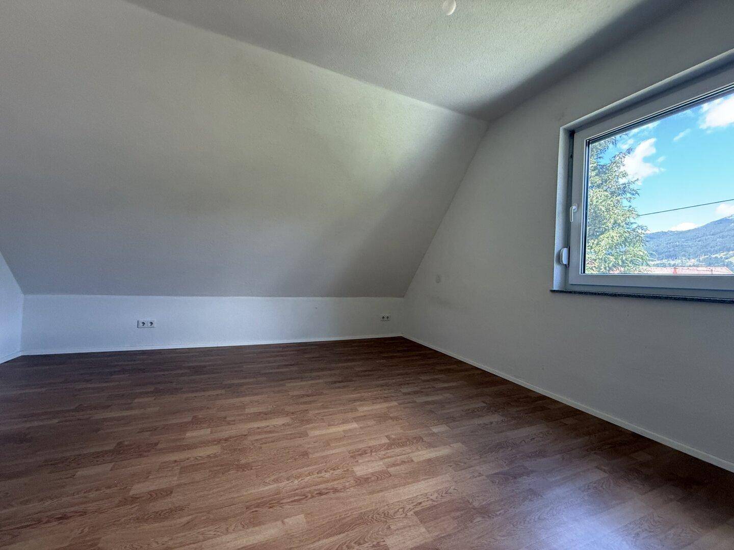 Helles Schlafzimmer mit Laminatboden, Dachschrägen und Fenster mit Bergblick.