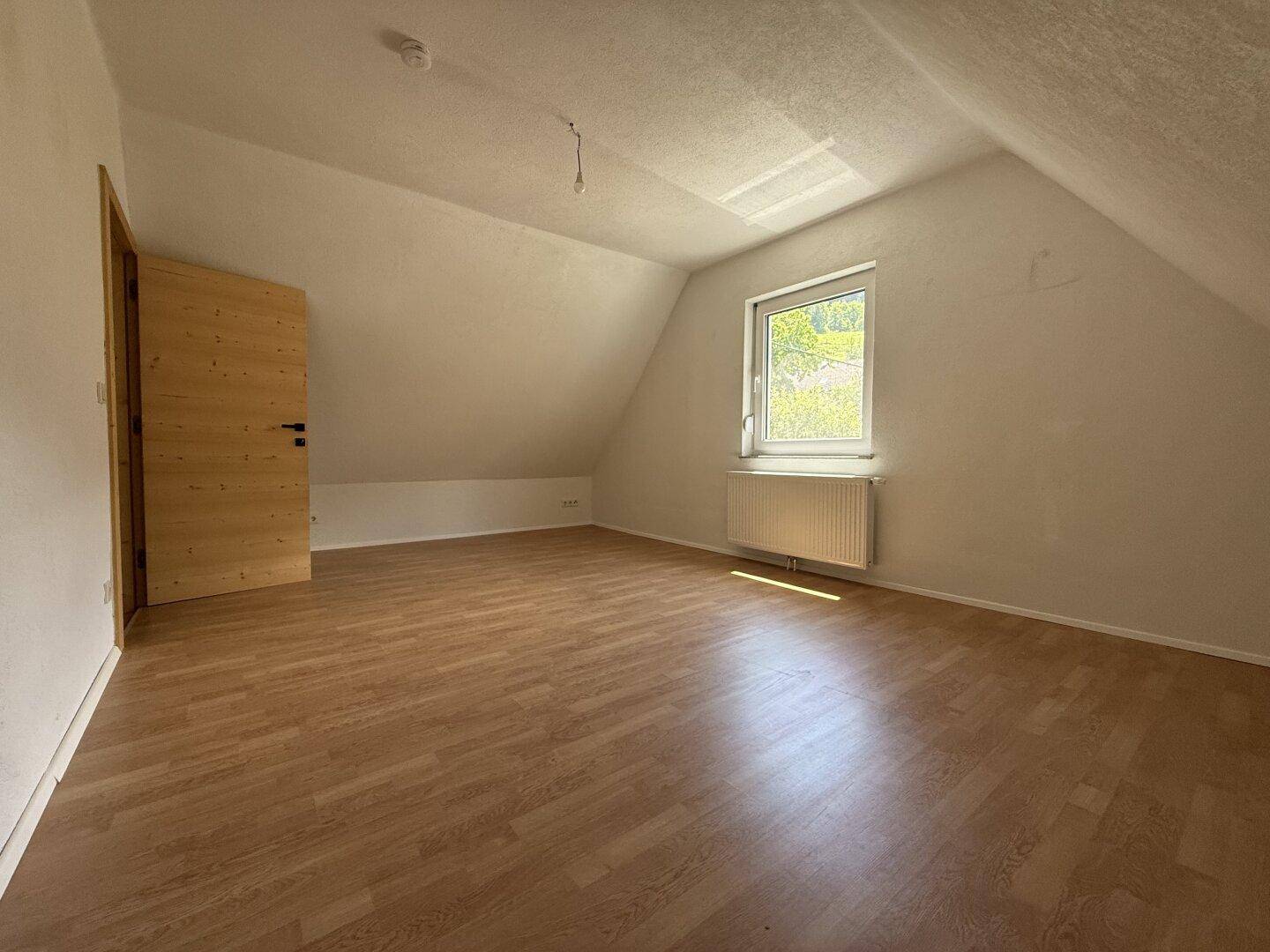 Helles Schlafzimmer mit Laminatboden, Dachschrägen und Fenster mit Blick ins Grüne.