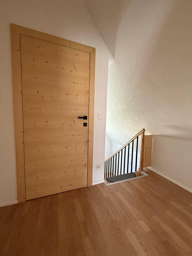Heller Raum mit Holzboden, Holztür und Zugang zu einer Treppe.